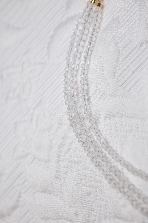 Zbliżenie na trzy rzędy transparentnych kryształków tworzących delikatną kolię na jasnej, teksturowanej tkaninie.